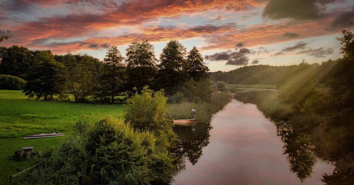 Een rustig water met groene oevers en bomen bij een kleurrijke zonsondergang